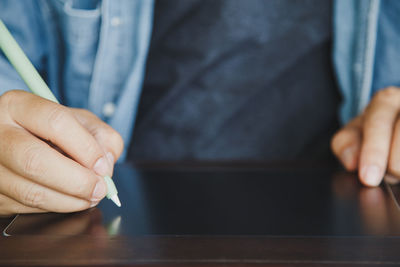 Close up a man in casual clothes using an electronic pen on a blank tablet on the wooden table