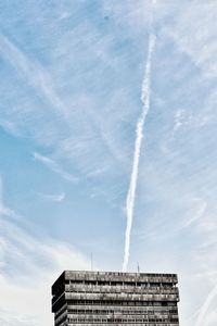 Low angle view of building against vapor trail in sky