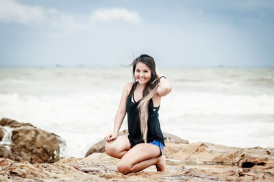 Young woman sitting on shore at beach against sky