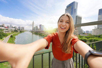 Happy smiling girl takes self portrait with ponte estaiada bridge and cityscape of sao paulo, brazil