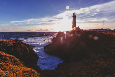 Lighthouse by sea against sky during sunset