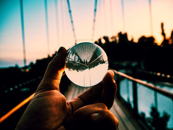 Close-up of hand holding crystal ball against sky during sunset