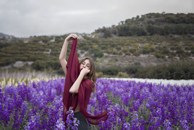 Young woman with eyes closed standing amidst purple flowers on field