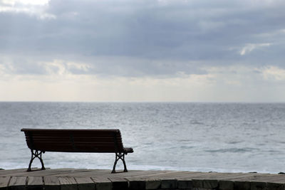 Empty bench by sea against sky