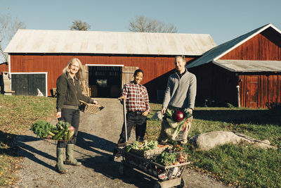 Portrait of multi-ethnic male and female farmers with organic vegetables standing outside barn