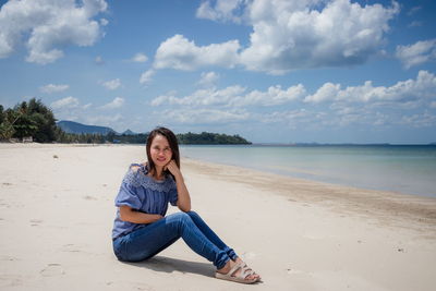 Portrait of woman sitting at beach against sky