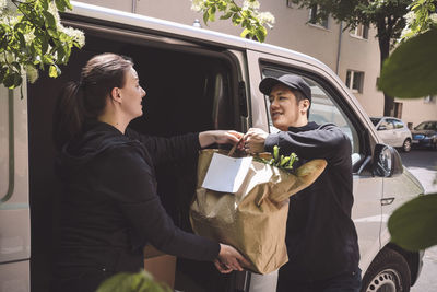 Delivery man talking to female coworker while holding package bag near truck