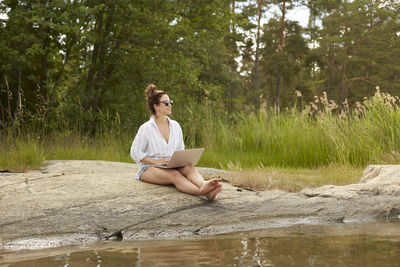 Woman using laptop at lake barefoot