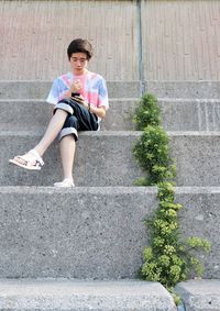 Full length of teenage boy using mobile phone while sitting on steps