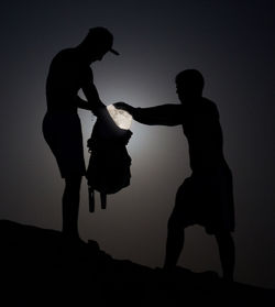Optical illusion of silhouette men putting moon in bag