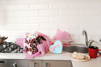 Bouquet of spring flowers on kitchen table with gift box.