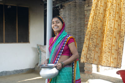 Woman in sari holding kitchenware looking at camera