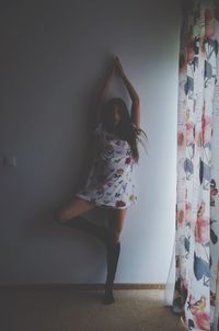 Portrait of young woman with arms raised standing at home