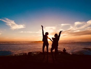 Silhouette friends standing at beach against sky during sunset