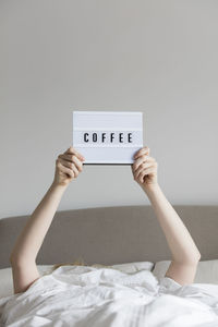 Cropped hand of woman holding text while lying on bed