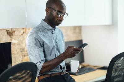 Businessman with coffee mug using mobile phone at workplace