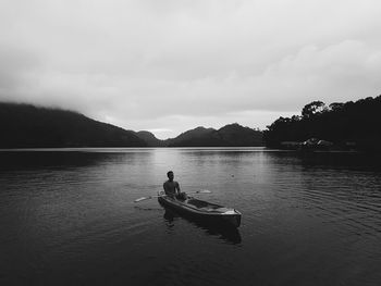 Man boating on lake against cloudy sky during sunset