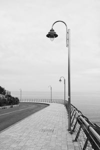 Street light on footpath by sea against sky