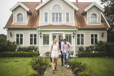 Happy multi-ethnic friends walking on footpath against villa during weekend