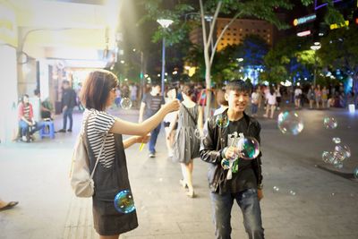 Happy teenage boy and girl playing with bubbles on sidewalk in city