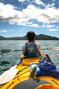 Rear view of man sitting in sea against sky