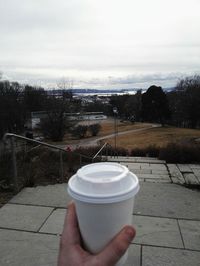 Close-up of hand holding tea cup against sky