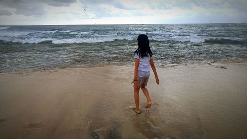 Girl walking at beach against sky