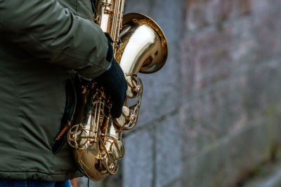 Midsection of man holding musical instrument while standing by wall