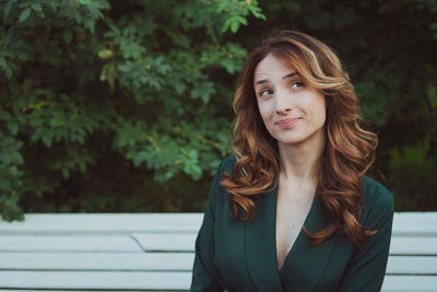 A young adult brunette woman is sitting on a bench in a green dress.