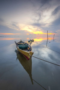 Fishing boat moored in sea against sky during sunset