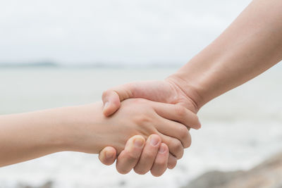 Close-up of people holding hands against sea and sky