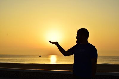 Man gesturing while standing against sea during sunset