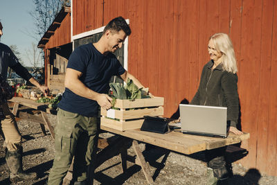 Mid adult man buying vegetables full of crate from female farmer at market