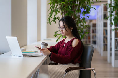 Student girl procrastinate in library with smartphone chat in social media not preparing for exam