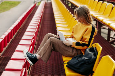 A young girl is doing her homework using a laptop in the stands of the stadium. 