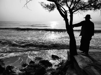 Silhouette man standing on rock at beach against sky