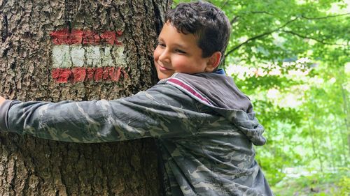 Portrait of boy standing by tree trunk hugging tree