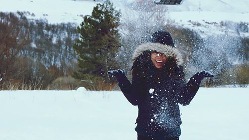 Cheerful woman throwing snow against trees