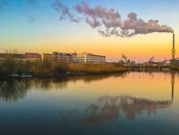 Scenic view of lake by buildings against sky during sunset