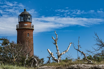 Dead trees by lighthouse against sky