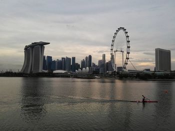 Man kayaking in sea by marina bay sands and singapore flyer against cloudy sky during sunset