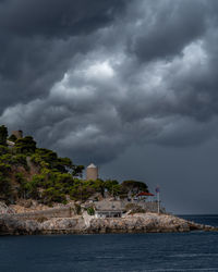 Building by sea against storm clouds