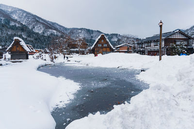 Houses on snow covered field by buildings against sky