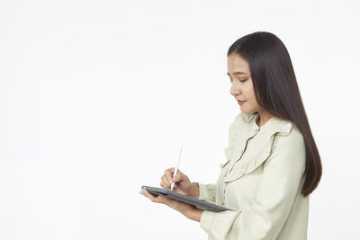 Side view of young woman using smart phone against white background