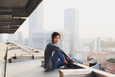 Portrait of woman sitting against buildings in city