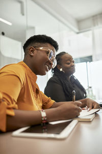 Smiling female professional making notes by colleague during meeting at coworking office