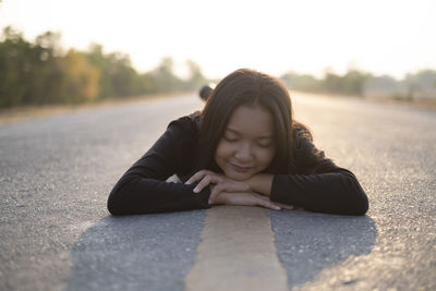 Portrait of young woman lying on road