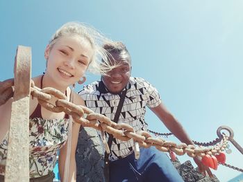 Portrait of young man and woman by railing against clear sky