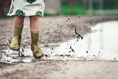 Low section of girl jumping in puddle on road