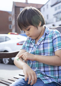 Cute boy looking away while sitting on car